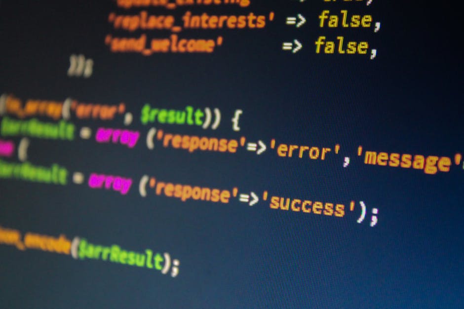 A close-up photograph of a computer screen displaying colorful lines of HTML and CSS code, with a person's finger partially visible in the foreground pointing towards the right side of the screen. The